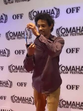 Nathan Hewitt holding his award in front of the Omaha Film Festival backdrop